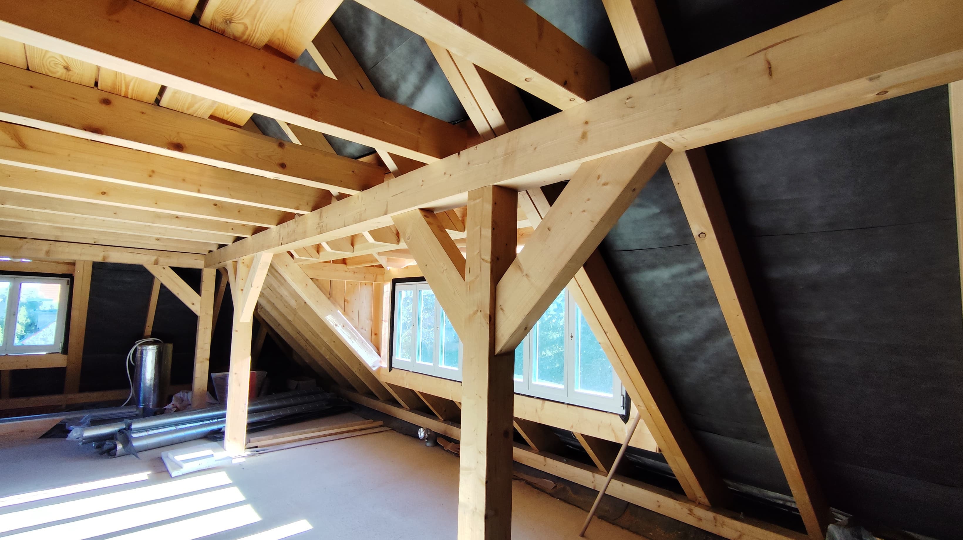 Offener Dachstuhl mit Holzsparren und Dachfenstern während des Dachausbaus im Rohbau